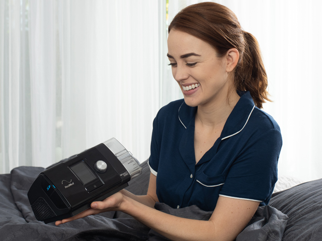 Smiling woman holding her ResMed AirSense 10 CPAP machine