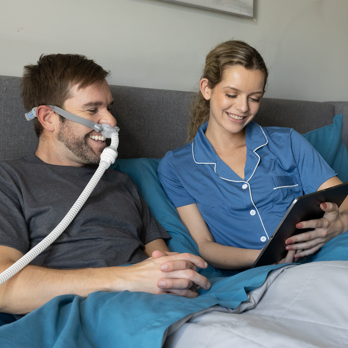 Couple smiling in bed, man wearing CPAP mask