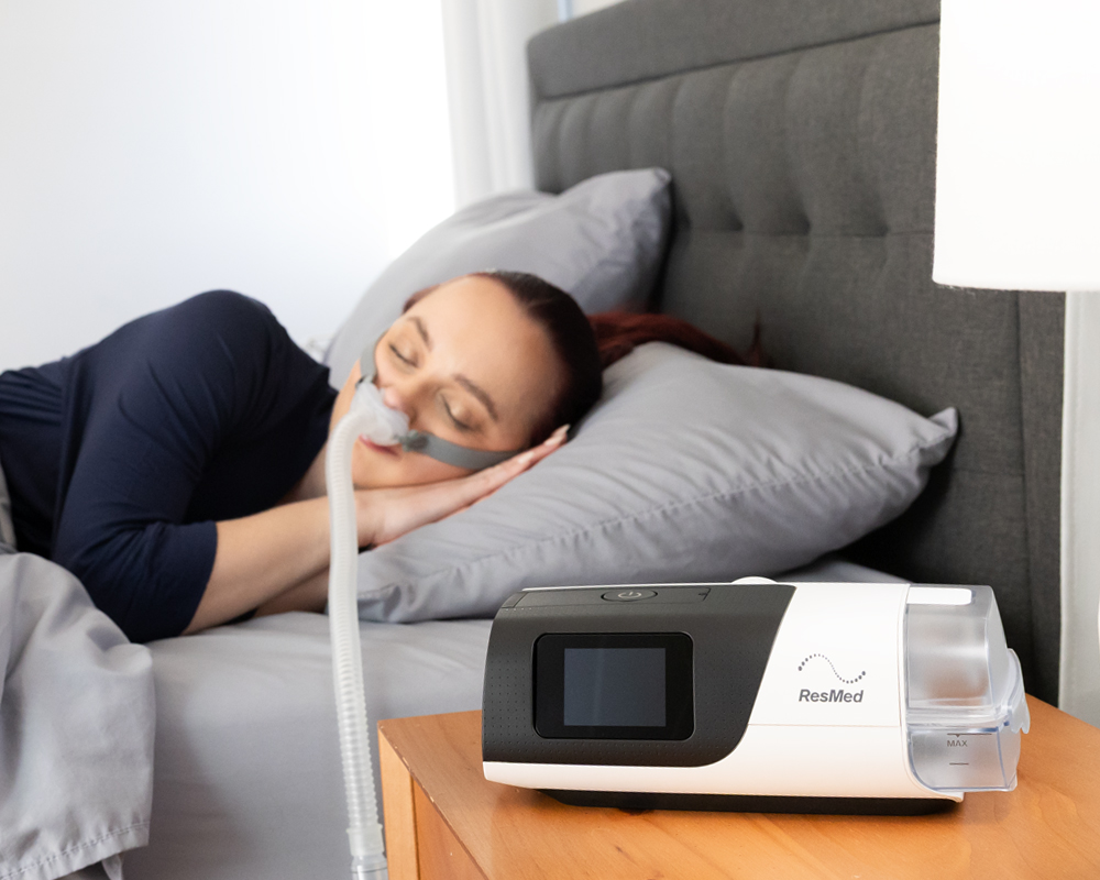Woman sleeping peacefully with CPAP mask next to ResMed machine