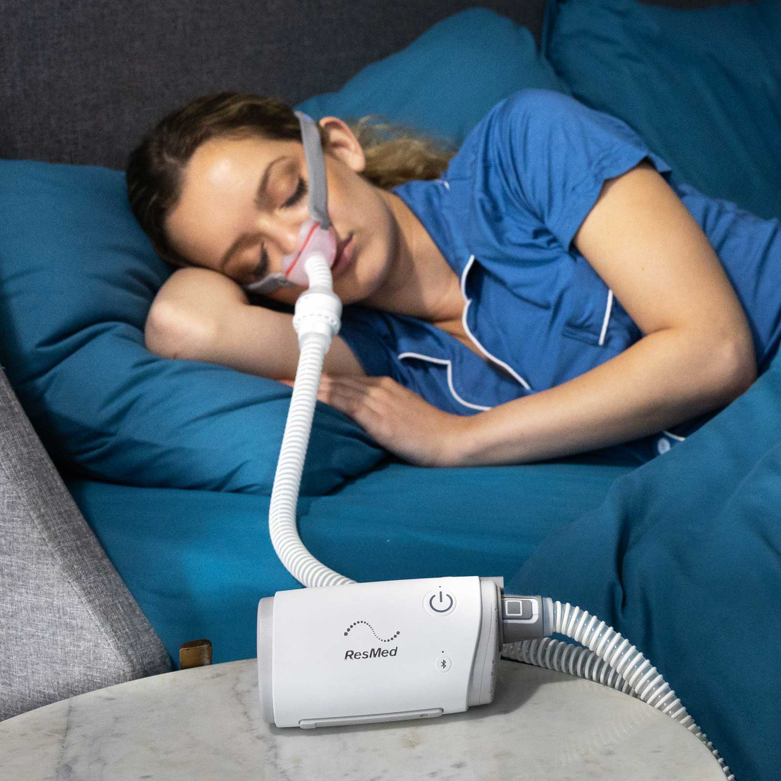 Woman sleeping peacefully with ResMed CPAP on bedside table