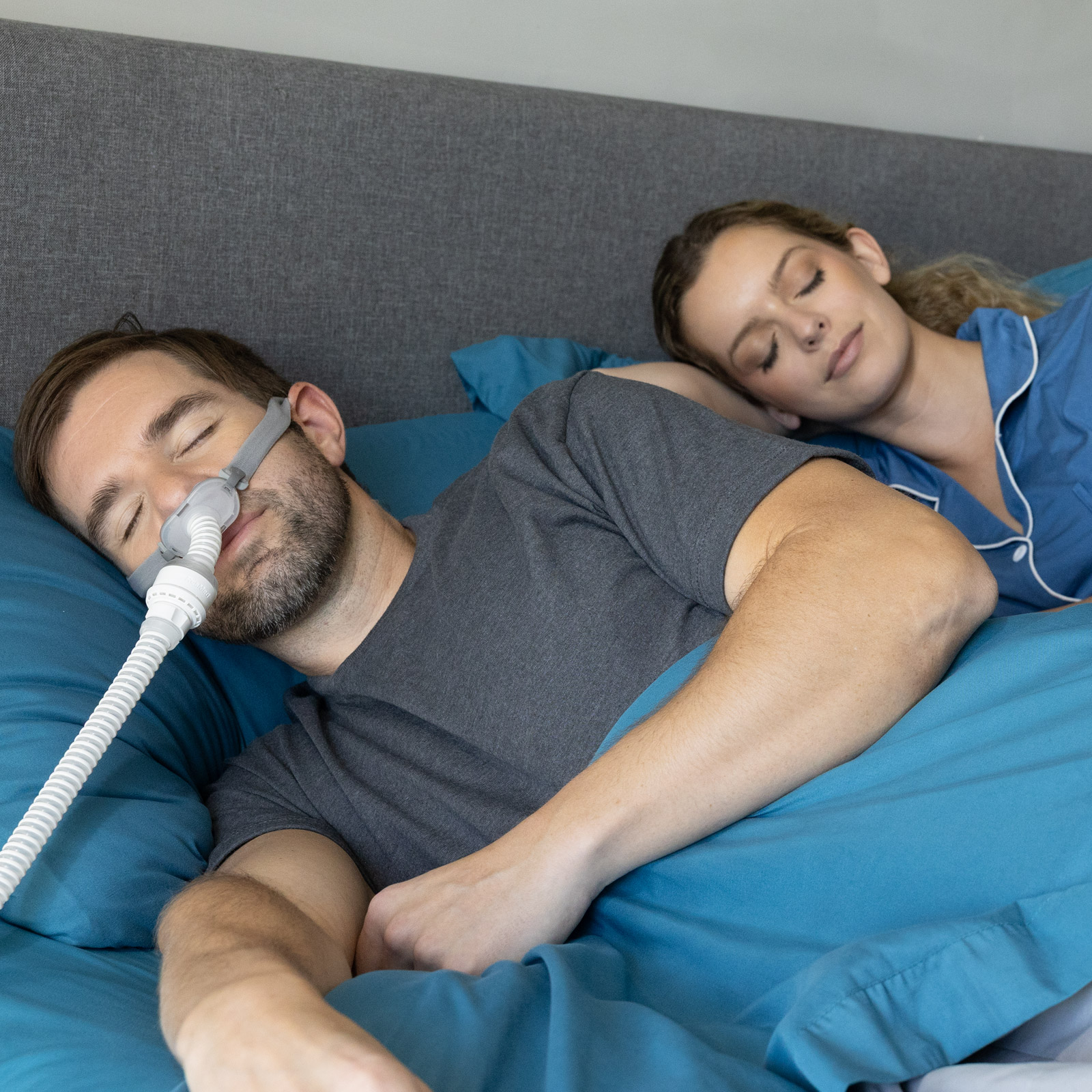 Couple sleeping peacefully in bed, partner wearing a CPAP nasal mask